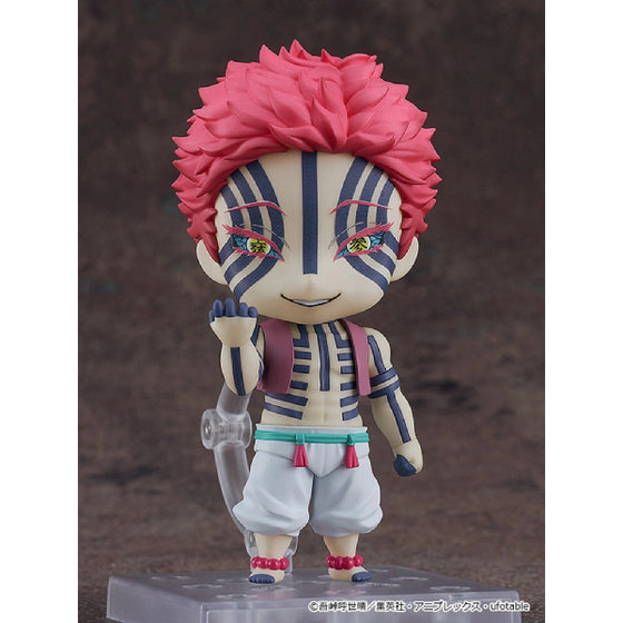 A Nendoroid action figure of Akaza from the anime series 'Demon Slayer', with a smiling face, wearing a white and pink outfit, holding a staff, and displaying a serious expression.